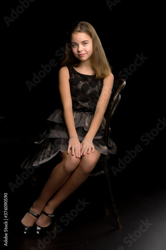 Portrait of a little girl sitting on an old Viennese chair, black background.