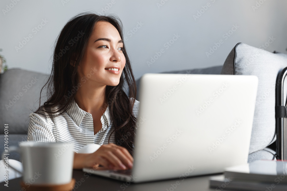 Close-up of ambitious beautiful asian female employee working from home. Girl on remote using laptop, smiling dreamy while looking outside window. Student feel inspired writing essay Close-up of ambitious beautiful asian female employee working from home. Girl on remote using laptop, smiling dreamy while looking outside window. Student feel inspired writing essay
