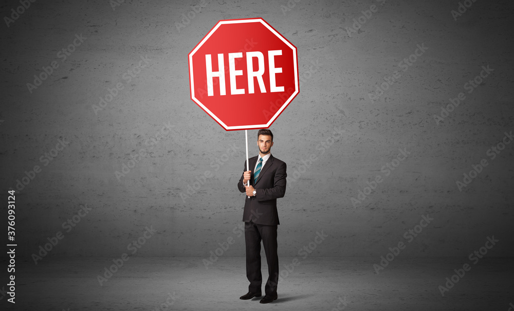 Young business person holding road sign with HERE inscription, new rules concept Young business person holding road sign with HERE inscription, new rules concept