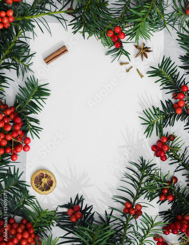 Round frame created from red mountain ash and green fir branches on white Christmas background. Closeup. Empty place for inspirational wishes text, quote or sayings. New Year's composition. 