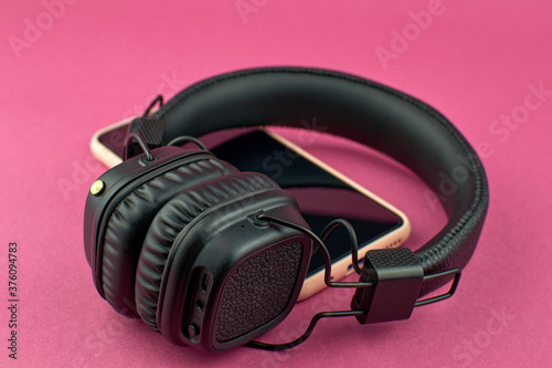 Wireless black headphones and smartphone. Black over-ear headphones on pink background, soft focus