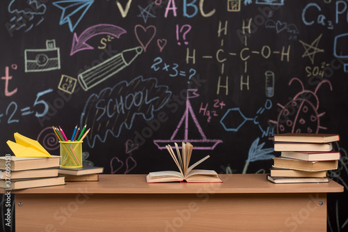 a desk with books and pencils against the background of a slate wall with drawings. blackboard with formulas in the classroom.