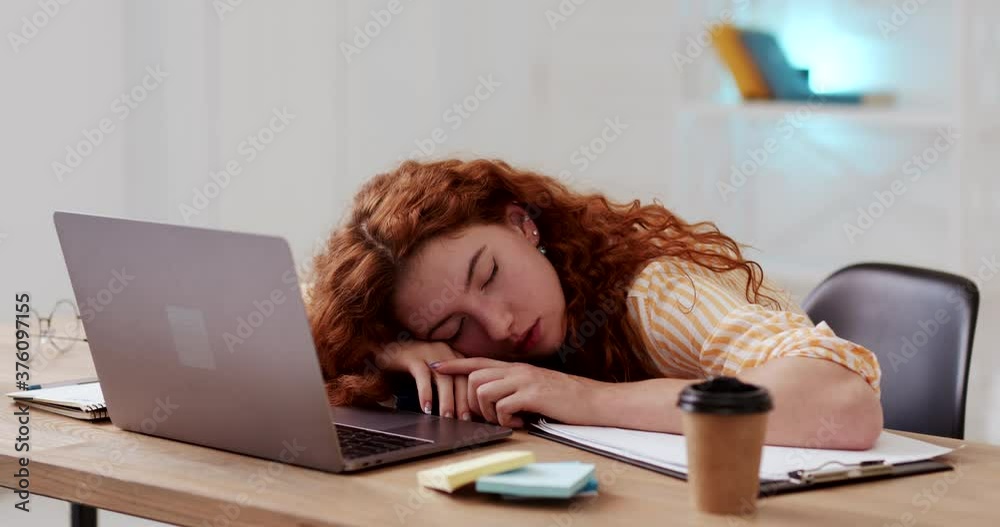 Calm relaxed young woman with red curly hair sleeping dozing peacefully on desk surface, tired of working studing on laptop, lying with head above hands. Calm relaxed young woman with red curly hair sleeping dozing peacefully on desk surface, tired of working studing on laptop, lying with head above hands.