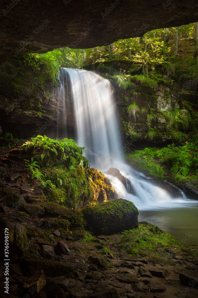 Obraz premium Amazing beauty of scenic waterfall called Skok (The Jump) in village on Old mountain called Senokos, framed by rocks and surrounded by sunlit green plants