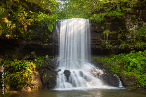 Amazing sunrays on scenic Skok waterfall, long exposure blurred motion of the water and vivid green plants on the wet, dark rocks