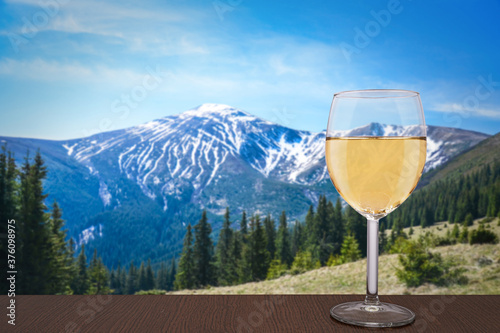 Glass of white wine with view of mountains in Ukraine. Beautiful view of rocks, forest and blue sky in Carpathian Mountains. Scenic mountain landscape.