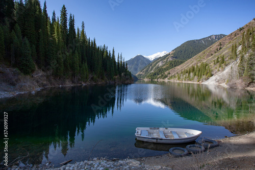 Alpine lake Kolsay in Kazakkhstan. The slopes of the mountains covered with coniferous forest are reflected in the water. A lone boat on the shore.