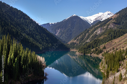 Alpine lake Kolsay in Kazakkhstan. Coniferous forest-covered mountain slopes are reflected in the water.