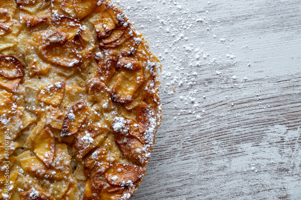 Homemade baking. Freshly baked apple pie on a light wooden background sprinkled with icing sugar.