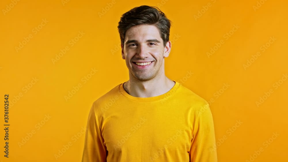 Handsome young man smiles to camera. Guy showing OK sign and winks over yellow background. Winner. Success. Body language. Handsome young man smiles to camera. Guy showing OK sign and winks over yellow background. Winner. Success. Body language.