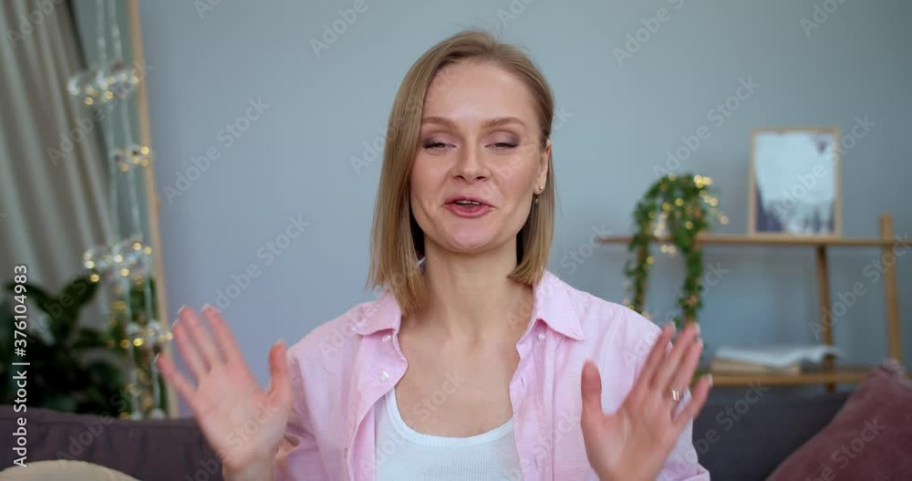 Woman influencer waving hello and showing thumb up while recording video for her beauty vlog. Cheerful girl talking and smiling while looking to camera and sitting on sofa. Woman influencer waving hello and showing thumb up while recording video for her beauty vlog. Cheerful girl talking and smiling while looking to camera and sitting on sofa.