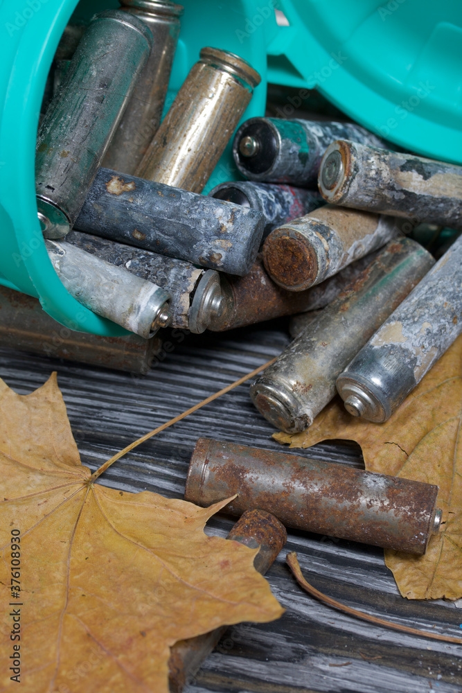 Corroded used batteries. They lie in and around an overturned trash can. Dried maple leaves lie nearby. Disposal of hazardous waste. Corroded used batteries. They lie in and around an overturned trash can. Dried maple leaves lie nearby. Disposal of hazardous waste.