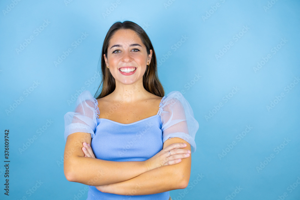 Young beautiful woman over isolated blue background smiling with her arms crossed
