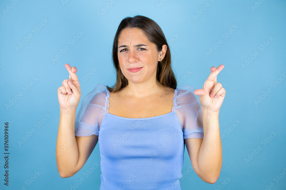 Young beautiful woman over isolated blue background gesturing finger crossed smiling with hope Young beautiful woman over isolated blue background gesturing finger crossed smiling with hope