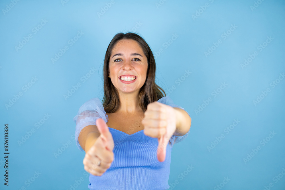 Young beautiful woman over isolated blue background Doing thumbs up and down, disagreement and agreement expression. Crazy conflict Young beautiful woman over isolated blue background Doing thumbs up and down, disagreement and agreement expression. Crazy conflict