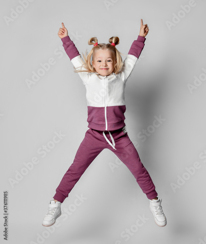 Fototapeta Naklejka Na Ścianę i Meble -  Cheerful baby girl in a stylish modern pink gray sports hoodie and pants jumps high.