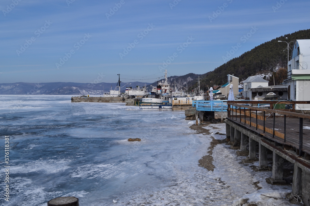 ships, port, mountains, iridescent crystals white blue ice  with cracks shine in the light the sun, the shore of lake Baikal in a snowy winter.
