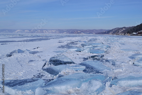 large iridescent crystals white blue ice floes with cracks glow in the light of the sun, lake baikal in winter, mountains on the horizon, blue sky, snow © SymbiosisArtmedia