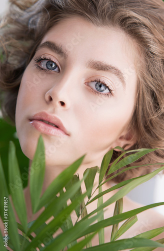 Beautiful young woman with perfect skin and natural make up. Teen model with green leaves. SPA and skincare.