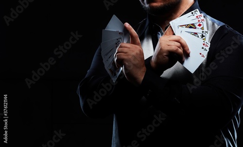 Magician illusionist showing performing card trick. Close up of hand and poker cards on black background. 