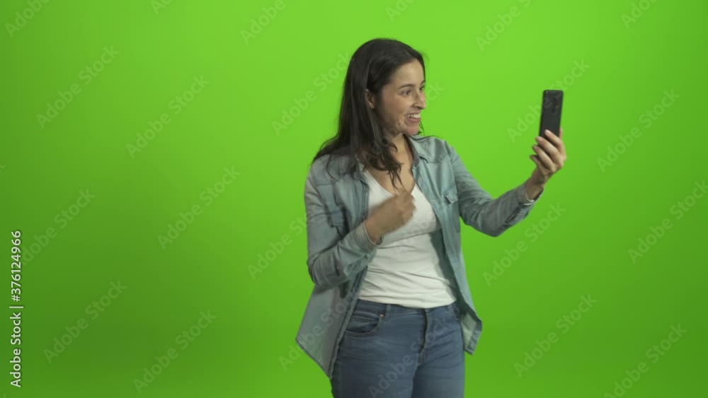 Smiling young woman on green screen blogger vlogger influencer speaking looking at mobile talking make video conference call record lifestyle blog vlog doing videochat mobile view
