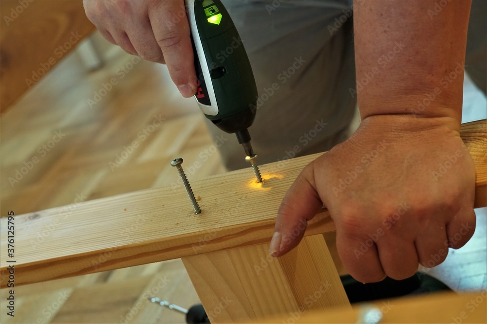 A man screwing screws in a wooden beams in assembling furniture as improvement of his home. He is using a power cordless screwdriver.