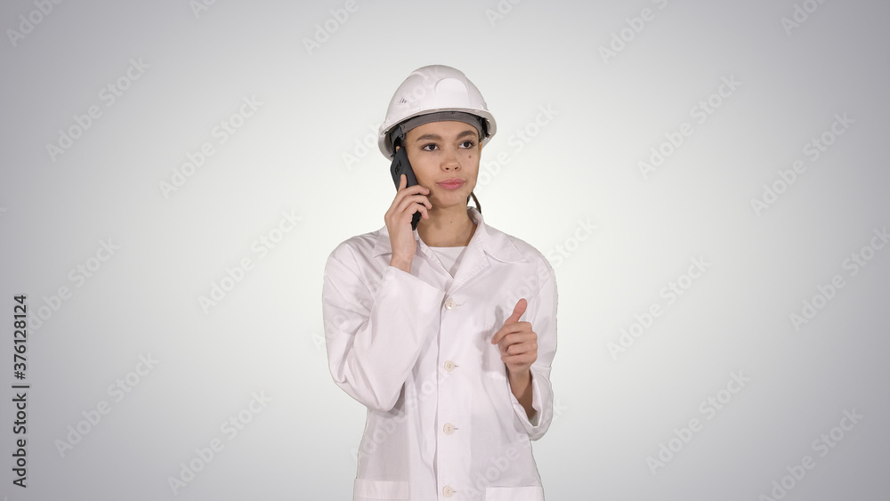 Woman engineer talking on the phone while walking on gradient background. Woman engineer talking on the phone while walking on gradient background.