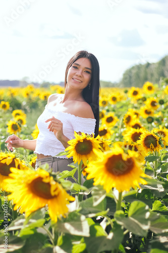 Beautiful brunette woman in a white top on the field with sunflowers. Yellow sunflowers. Close plan. © Sarbinaz Mustafina