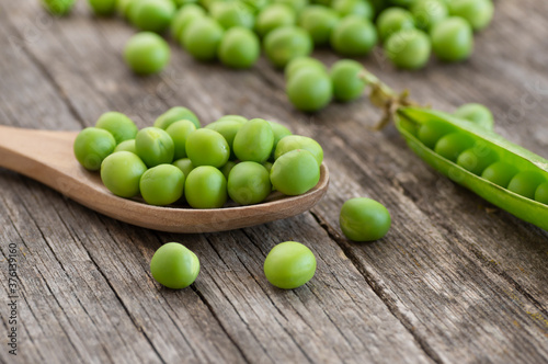Fresh green peas with pod in wooden spoon on wooden table, healthy green vegetable or legume ( pisum sativum )