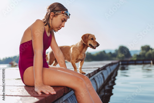 Girl sitting on the river dock with her dog