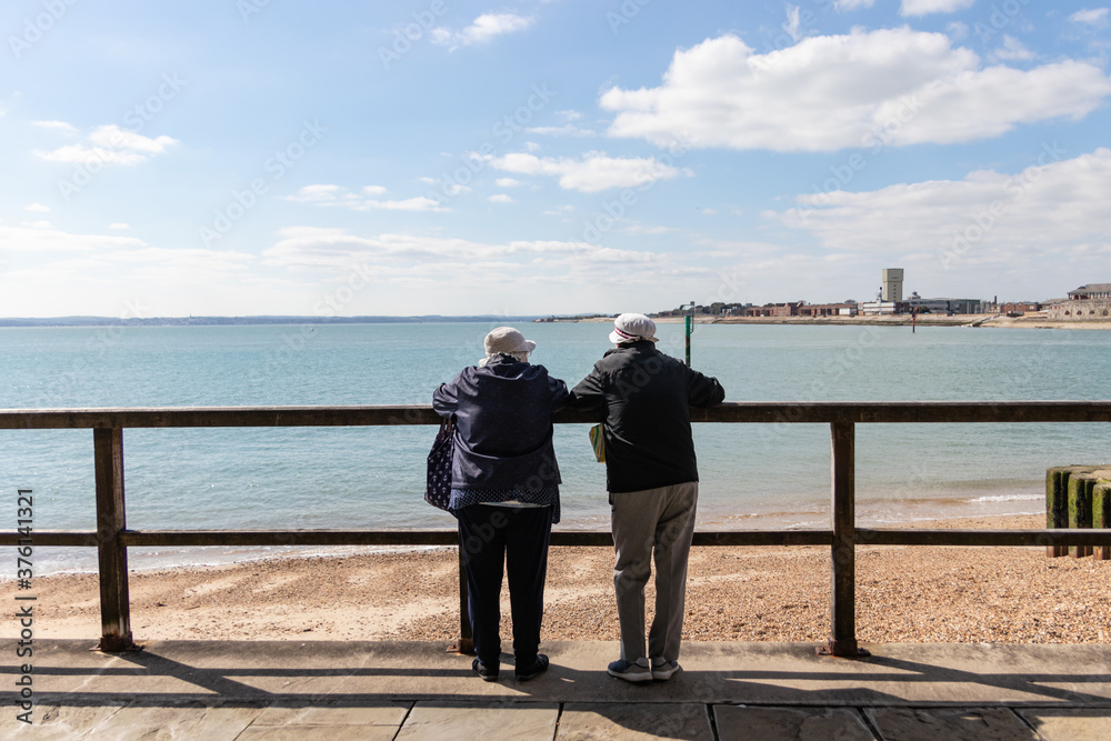 an elderly couple leaning on a fence looking at a view by the sea