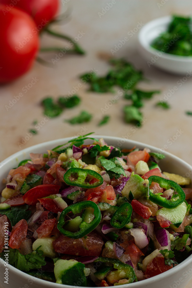 Kachumbari in a bowl with tomatoes and coriander in the background Kachumbari in a bowl with tomatoes and coriander in the background