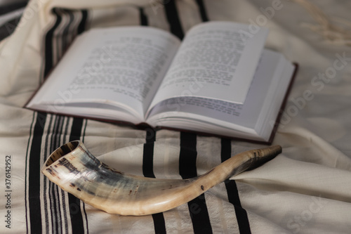 A shofar is placed on a tallit next to a Torah study book. Before the Jewish holidays of the month of Tishrei