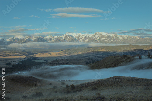 Morning landscape with a river valley  low clouds creeping on the ground and white snowy mountains in the background. Chuya ridge  Altai mountains  Siberia  Russia ..