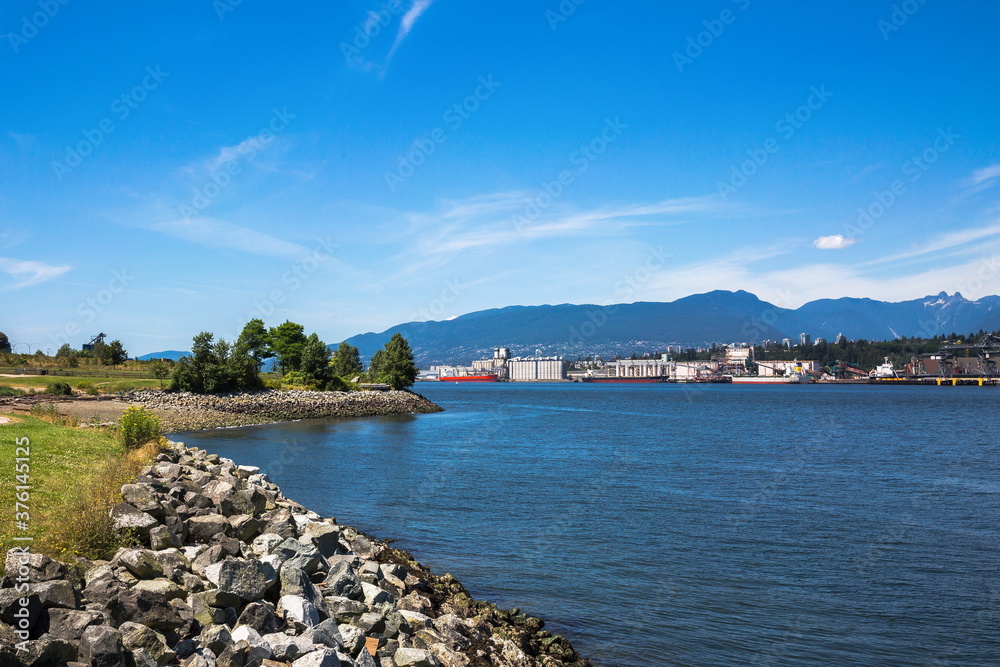 
View at  the seaport of North Vancouver from the parkland of Burnaby City. Ships loading at the seaport of North Vancouver against the backdrop of a mountain range and blue sky
