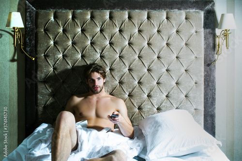 Carefree guy enjoying morning. Shirtless man in bedroom. Handsome man in underwear sitting on bed.