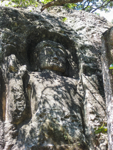Buddha carved on mountain rock cliff “ The large unfinished Buddha image at Dhowa Raja Maha Vihara or The Dhowa rock temple in Badulla District , Uva Province, Sri Lanka photo