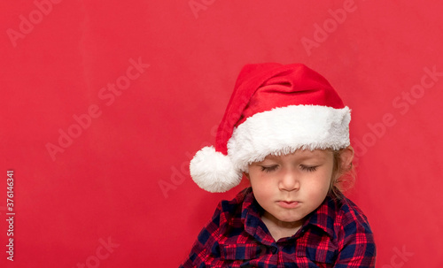  little girl with closed eyes in red Santa hat on a red background. portrait. Merry Christmas and Happy Holidays.