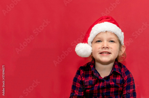 little girl in red Santa hat on a red background. portrait. Merry Christmas and Happy Holidays.