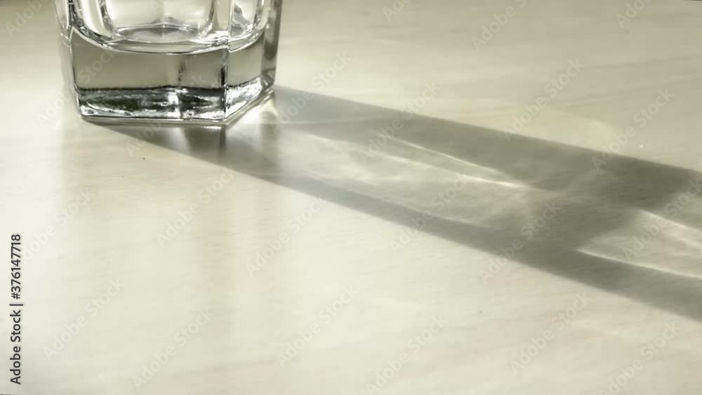 Time lapse of caustics in a drinking glass moving of a light wooden surface