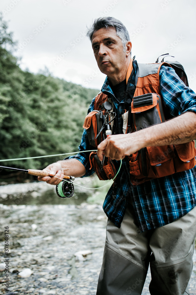 Senior man is fishing alone on fast mountain river. Active people and sport fly fishing concept. Senior man is fishing alone on fast mountain river. Active people and sport fly fishing concept.
