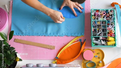 skilled seamstress draws sewing patterns of cosmetic bag parts on light blue fabric with chalk at workplace close upper view photo