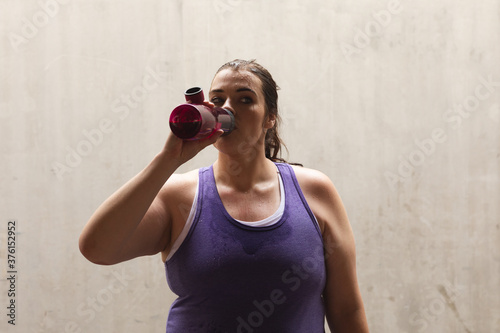 Curvy Caucasian woman drinking from a water bottle during her workout