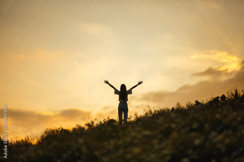 silhouette of happy woman relaxing on mountain hill  in summer sunset sky happy girl enjoying freedom and life raising arms feeling free
