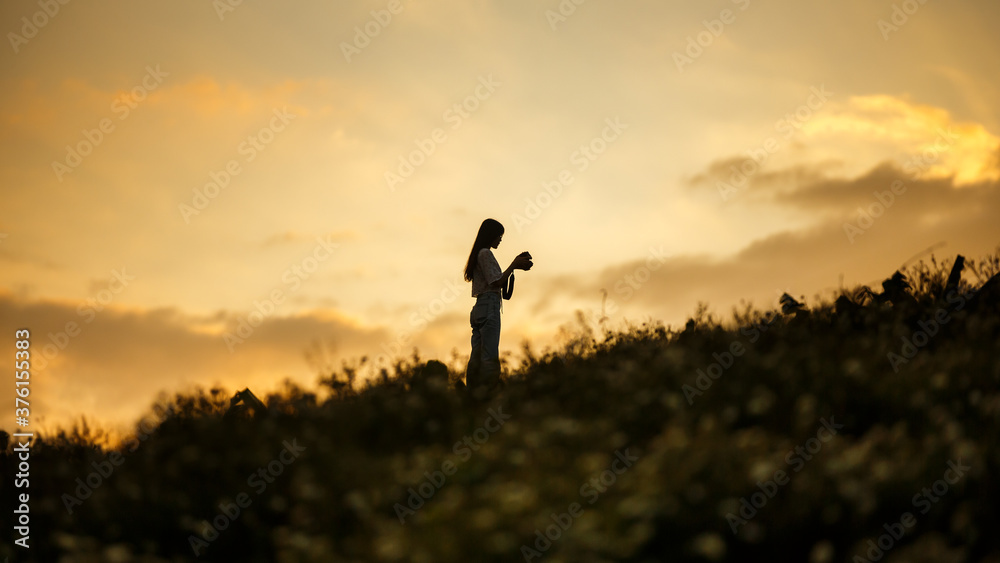 Silhouette of  woman holding camera on the hill at sunset 