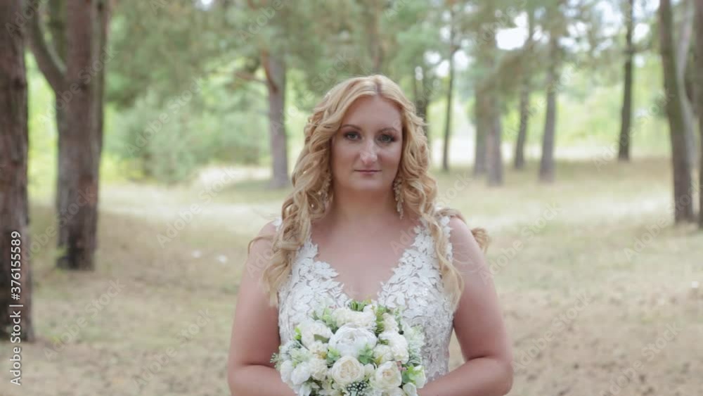 Bride with wedding bouquet in green summer forest.