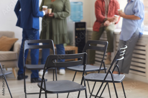 Cropped shot of empty chairs in circle during support group meeting with people chatting in background, copy space