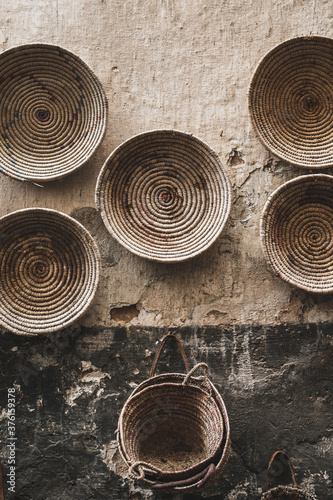 Handmade wicker round baskets hanging on textured wall in Marrakech medina souk. Traditional moroccan manufacture. Grand Bazaar.