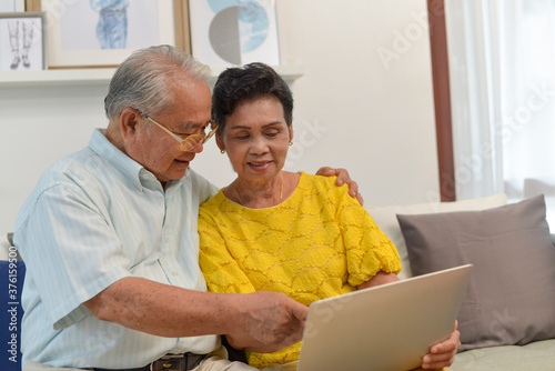 grandfather and grandmother used laptop to see photo or shopping on line in living room.Senior family concept.