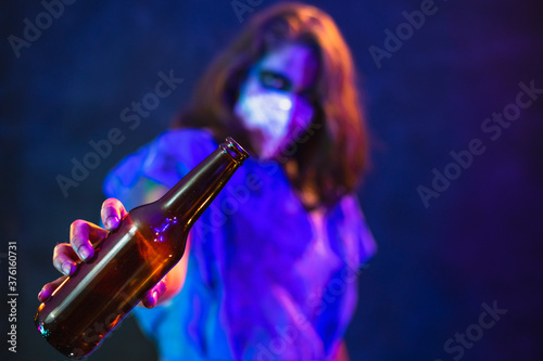 Halloween zombie with coronavirus Woman wearing face mask protective for Covid-19 holding a beer botthe. Horror infection concept